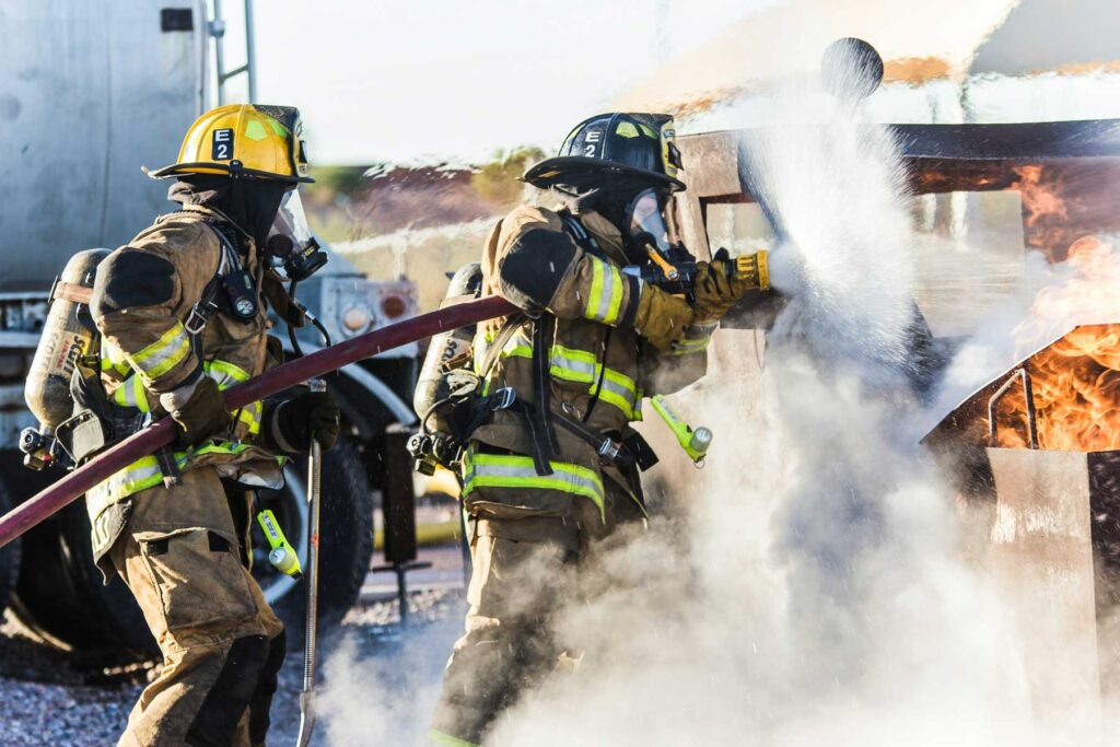 two fire fighters use water to extinguish a vehicle fire